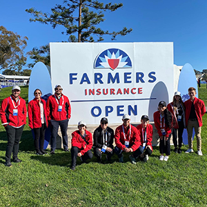 SMBA '22 cohort standing and sitting in front of the Farmers Insurance Open sign.