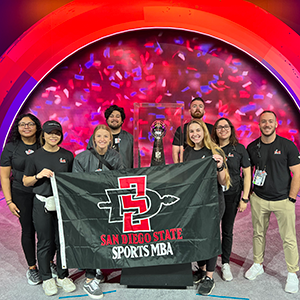 Sports MBA Area Managers standing with the Vince Lombardi trophy and holding SDSU Sports MBA flag
