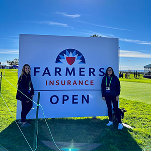 SMBA Students Sara Johnsen (left) and Astrid Enciso (right) in front of the Farmers Insurance Open sign.