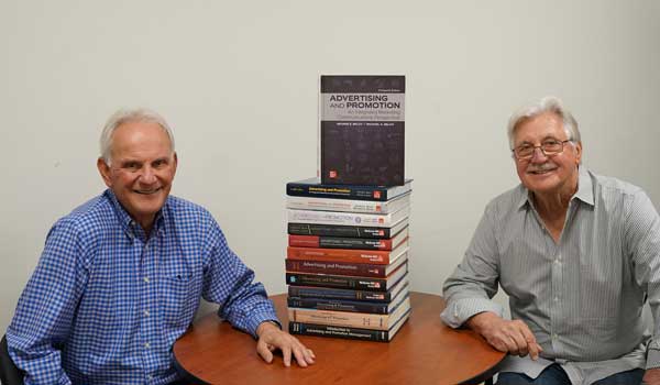 George Belch (left) and Michael Belch sit next to all 13 editions of their textbook